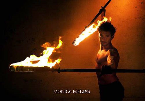 Un jongleur-cracheur de feu dans une position de combat face aux flammes