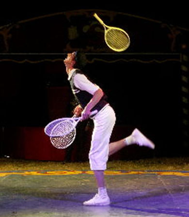 Le jongleur envoie des raquettes de tennis en l'air en s'aidant de ses jambes