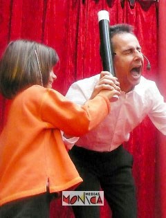 Un magicien sur scene lance un tour avec sa baguette geante et l aide d un enfant du public