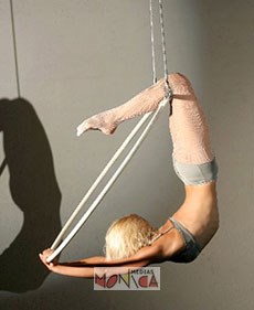 Artiste feminine accomplissant une figure sur un trapeze fixe de cirque suspendue par les jambes à la barre