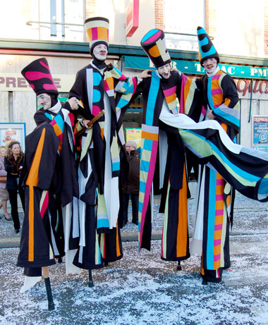 Quatre comediens echassiers farceurs stoppent leur marche pour le plaisir du public