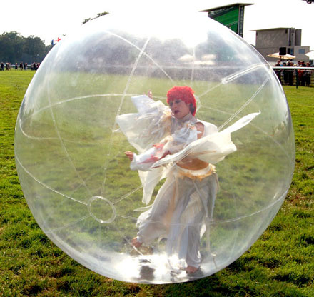 Une danseuse vetue de blanc est dans une grosse bulle artificielle pour un spectacle deambulatoire sur herbe