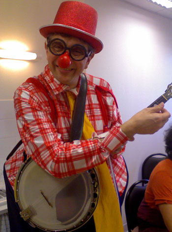 Un clown musicien avec son nez et chapeau rouge joue du banjo