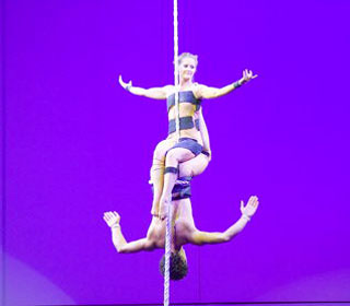 Une danseuse est assise sur son partenaire dont le corps est enroule a la corde lisse la tete en bas pour un spectacle aerien en duo