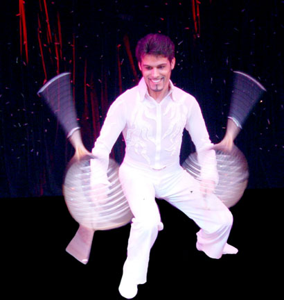 L'acrobate et jongleur Roggerio vetu tout de blanc fait tourner face a lui deux raquettes de tennis a une vitesse tres acceleree