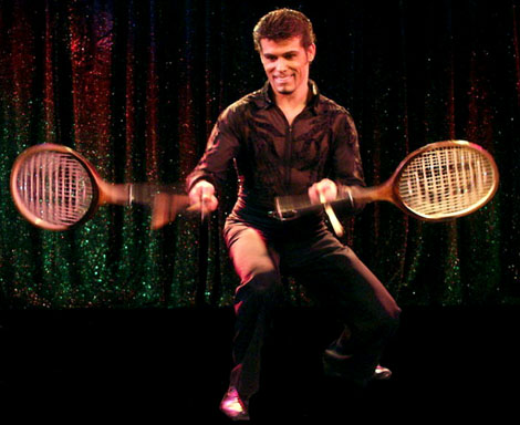 L'acrobate Roggerio vetu tout de noir jongle simultanement avec deux raquettes de tennis a l'aide de batons