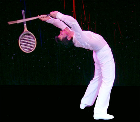 Cet acrobate se contorsionne pour jongler la tete en arriere avec ses deux raquettes de tennis
