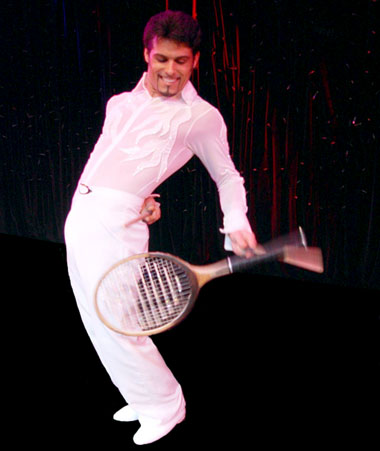 L'artiste jongleur realise une jonglerie avec ses raquettes dans son dos et toujours a l'aide de baguettes en bois
