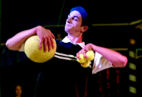 Ce jongleur serre trois petites balles de tennis dans sa main gauche et un ballon dans l'autre main pour son show de jonglerie