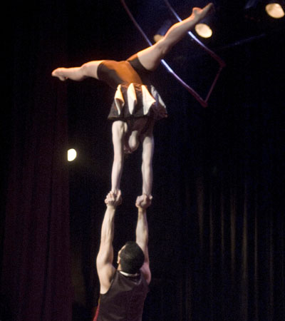 Un gymnste soutient sa partenaire en hauteur qui realise un grand ecart lors d'un spectacle de main a main