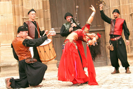 Une danseuse vetue de rouge danse courbee devant quatre musiciens du moyen age pour une grande fete medievale