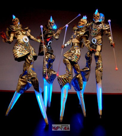 Quatre echassiers lumineux du futur portent des costumes de couleur or qui s'eclairent dans la nuit