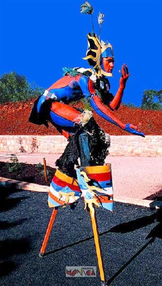 Le sorcier  aux couleurs indiennes se baisse sur ses echasses pendant le spectacle