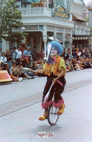 Greg le jongleur sur monocycle en costume colore avec des massues