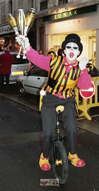 Cet artiste avec son masque de clown se tient sur son monocycle avec a sa main droite trois massues dorees