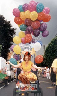 Artiste du cirque paradant dans la rue sur un triporteur sonorise et invitant à la fete des ballons et des chansons