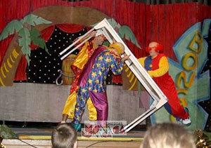Trio de clowns se débattant avec une grande table sur scene de theatre