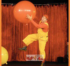 Un clown en salopette s'envole avec un ballon rouge geant sur une scene de theatre pour enfants