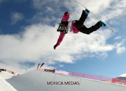 Un snowboarder en pleine torsion realise un grab sur un halfpipe tete en bas avec un bras appuye sur la neige