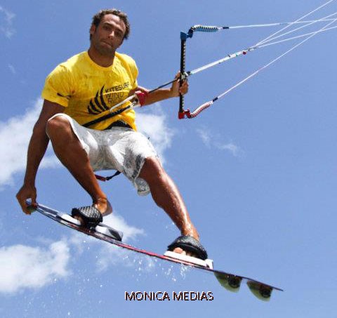 Un kitesurfeur realise un saut en l'air sous un ciel bleu avec la main serree contre la planche 
