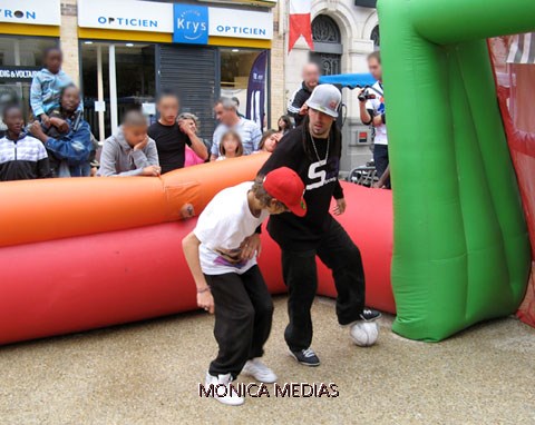 Des joueurs professionnels de street soccer avec des enfants lors d'une animation de foot sur un terrain en gazon